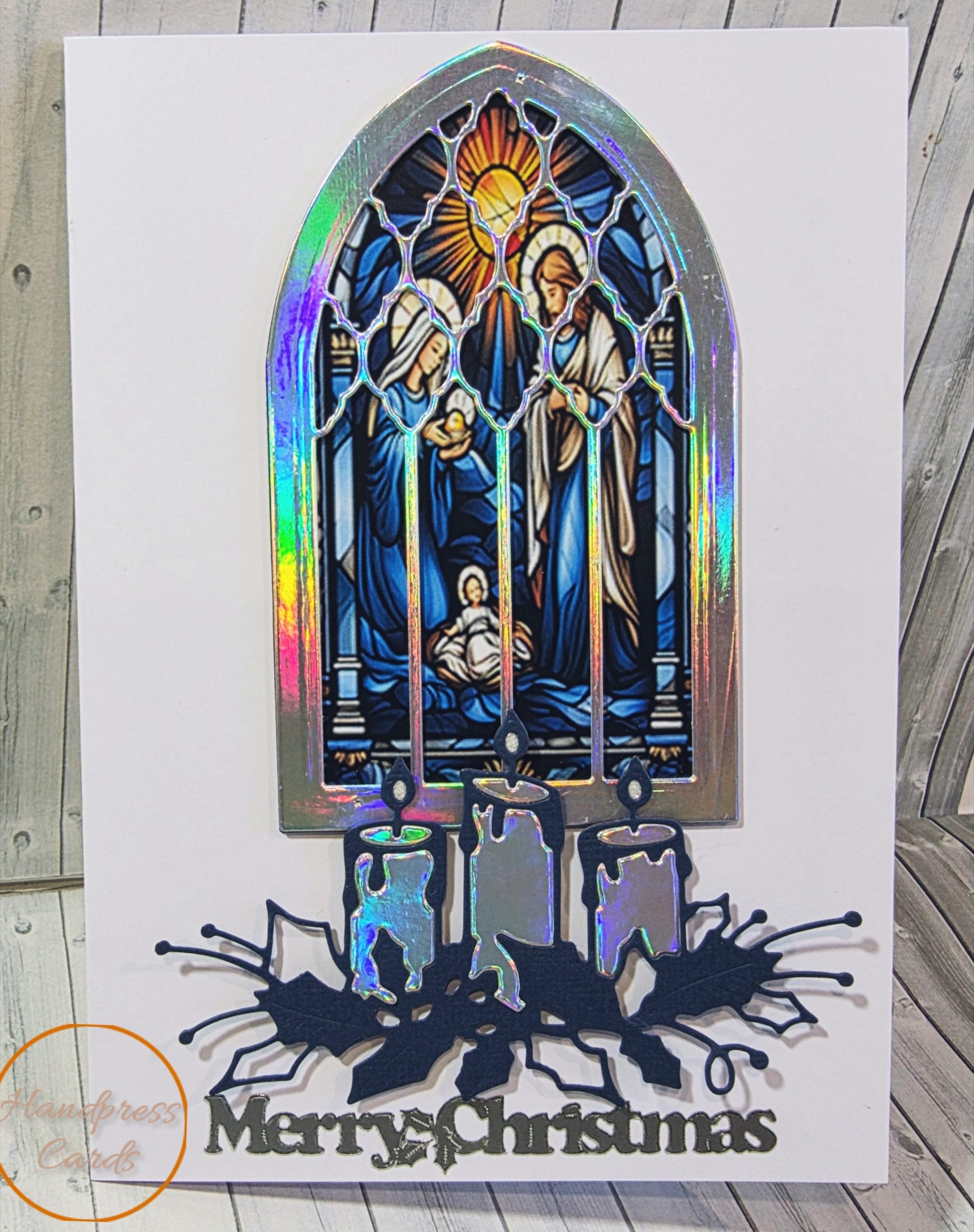 Handmade nativity Christmas card with a stained glass style Holy Family scene in a holographic foil arched window, foil candles, navy holly and a silver Merry Christmas sentiment