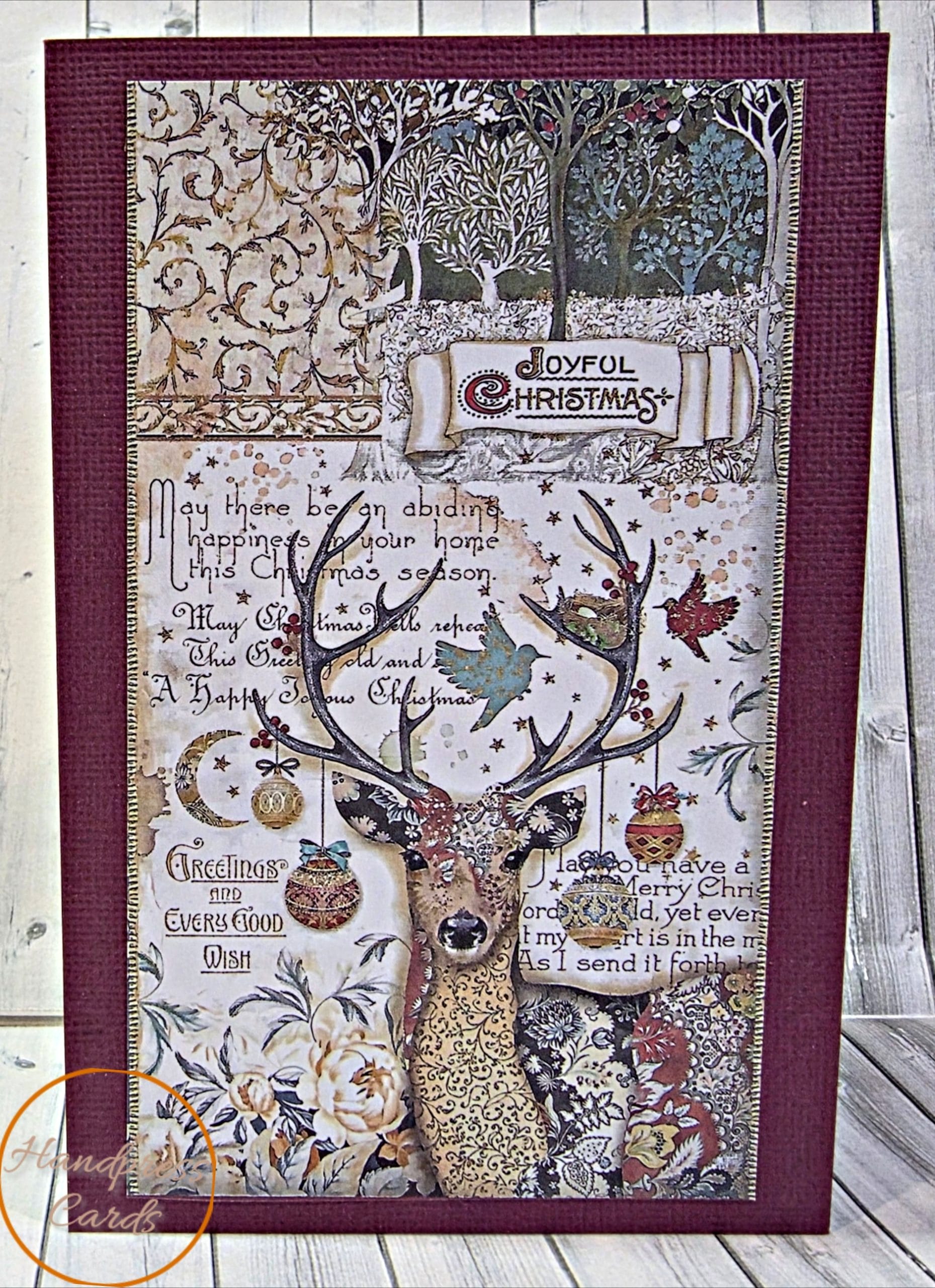 Handmade vintage Christmas card with a patterned stag, baubles, birds and a Joyful Christmas banner on a burgundy textured card
